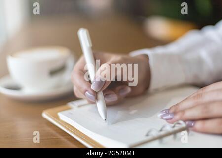 Closeup female hands making paper notes in notepad use pen table cafeteria writing diary, planning Stock Photo