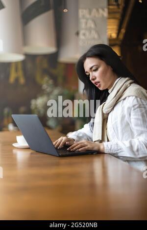 Focused mixed race business woman working remotely use laptop sitting at cafe table Stock Photo