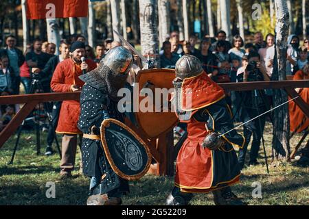 An epic sword battle. Two knights in armor and helmets, with shields in the arena. Imitation of medieval jousting tournaments. Bishkek, Kyrgyzstan - October 13, 2019 Stock Photo