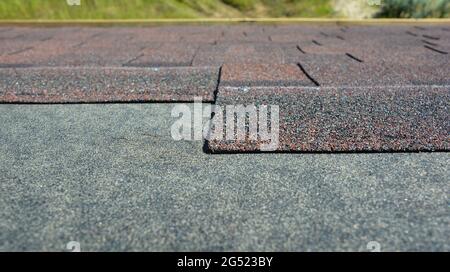 Asphalt roofing shingles installation: A close-up on the architectural asphalt, bitumen roofing shingles installed over a waterproofing underlayment. Stock Photo