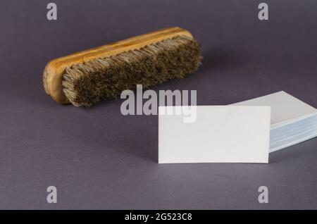 Garment cleaning brush and stack of blank business cards on gray background. Wooden brush with natural bristles and white rectangular business cards. Stock Photo