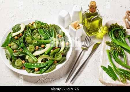 Green vegetable salad of sauteed tenderstem broccoli, snow peas, avocado, cucumber, chickpeas, baby spinach with olive oil dressing, served on a white Stock Photo