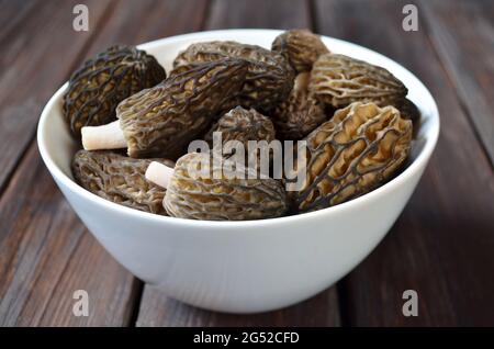 Bowl of freshly harvested spring morel mushrooms on a wooden table. Close-up, selective focus Stock Photo