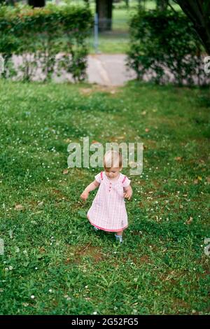Little girl in a dress walks on a green lawn Stock Photo