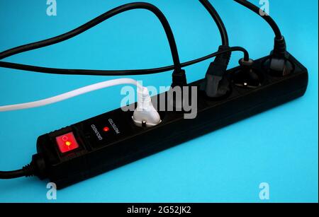 Black power surge protector with cables and light on blue background. Electrical power strip Extension socket, power extender, surge protector. Stock Photo