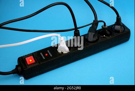 Black power surge protector with cables and light on blue background. Electrical power strip Extension socket, power extender, surge protector. Stock Photo