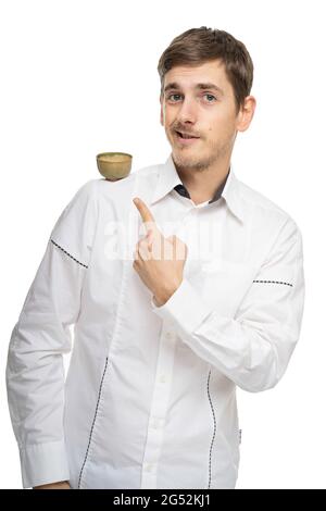 Young handsome tall slim white man with brown hair pointing at tea cup at his shoulder in white shirt isolated on white background Stock Photo