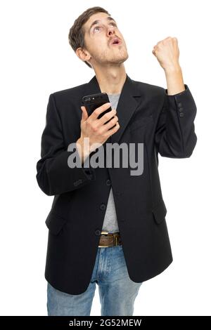 Young handsome tall slim white man with brown hair with mobile phone doing winning gesture in black blazer isolated on white background Stock Photo