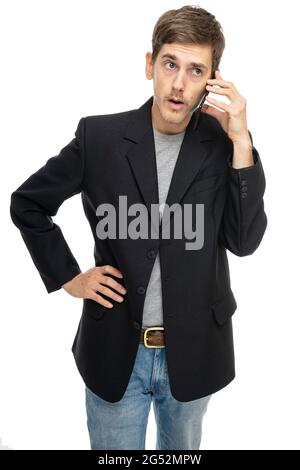 Young handsome tall slim white man with brown hair is on the phone in black blazer in blue jeans isolated on white background Stock Photo