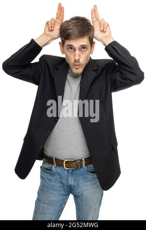 Young handsome tall slim white man with brown hair making bunny ears in black blazer in gray shirt isolated on white background Stock Photo