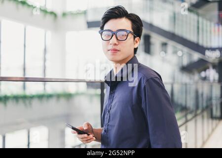 Portrait of an Asian businessman, confident and smiling, holding a phone in his hand Stock Photo