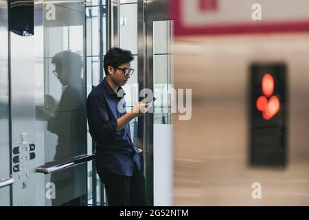 Hands of young Asian man, using smart mobile phone, in elevator Stock Photo