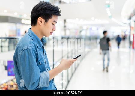 Hands of young Asian man, using smart mobile phone, at blurred shopping mall background. Stock Photo