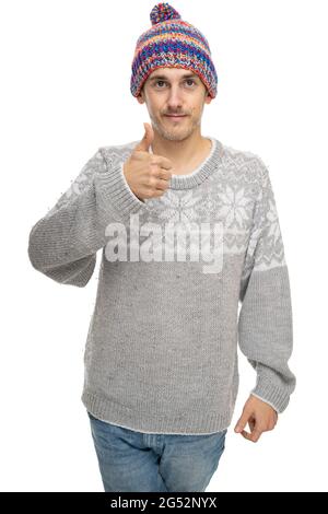 Young handsome tall slim white man with brown hair showing thumb up in gray jumper with colorful winter hat isolated on white background Stock Photo