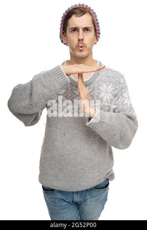 Young handsome tall slim white man with brown hair making time out gesture in gray jumper with colorful winter hat isolated on white background Stock Photo