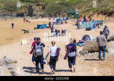 Staycation holidaymakers enjoying the sunshine on Mawgan Porth Beach in Cornwall in the UK; Families using colourful beach shelters and windbreaks.