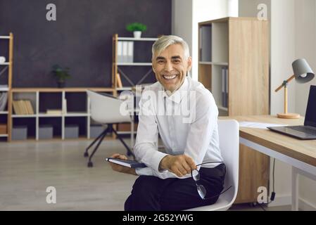 Portrait of happy mature businessman sitting on chair, smiling and looking at camera Stock Photo