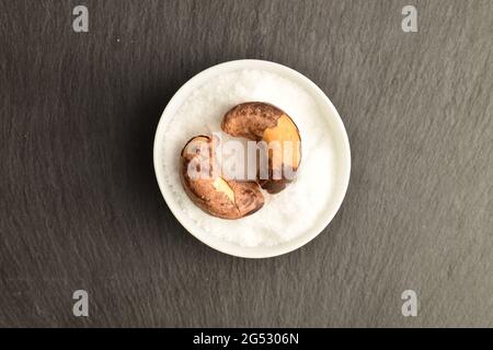Two roasted cashews in a salt shaker, close-up, on a slate board, top view. Stock Photo