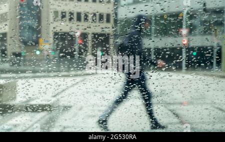 Stuttgart, Germany. 25th June, 2021. Raindrops collect on a window that a man walks past. Credit: Bernd Weißbrod/dpa/Alamy Live News Stock Photo