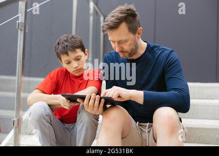 The teacher is engaged with boy on stairs using a mobile device - tablet. The concept of non-formal education in the style of urban life Stock Photo