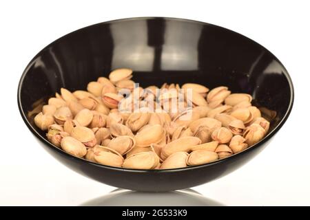 Delicious pistachios in a ceramic black plate, close-up, on a white background. Stock Photo