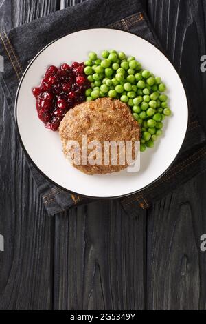 Veal burger with green peas and lingonberry jam close-up in a plate on the table. Vertical top view from above Stock Photo