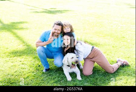 happy family portrait of mom dad and kid boy playing with pet in park on green grass, togetherness Stock Photo