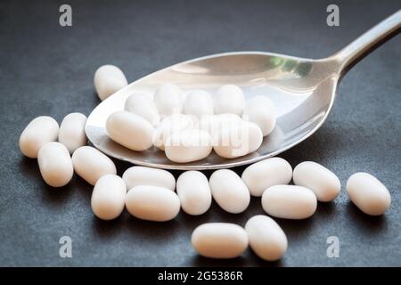 White pills in spoon on dark background. Stock Photo