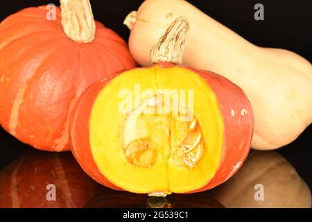 One ripe organic pumpkin cut and two whole, close-up isolated on black. Stock Photo