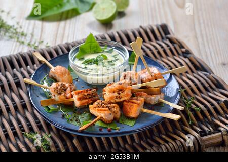 Grilled salmon skewers with roasted sesame seeds served on horseradish leaves and a mustard dip sauce Stock Photo