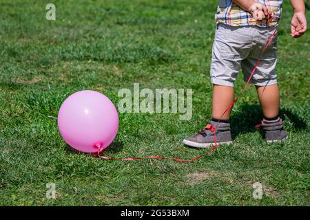 Rear view of toddler from the waist down holding a string tied to a pink balloon outside in a park Stock Photo