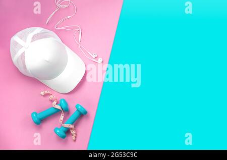 Flat lay of sports equipment on colored background. Top view of a blue and pink background with a cap, headphones, dumbbells and a measuring tape Stock Photo