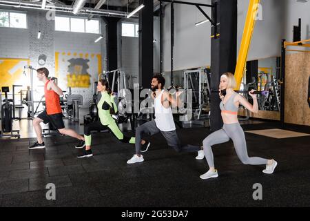 young multiethnic sports people doing forward lunges with gymnastic sticks Stock Photo