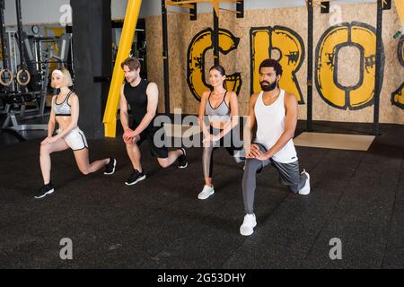 smiling interracial people doing forward lunge exercise in gym Stock Photo