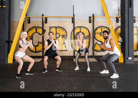 joyful multiethnic people doing sit ups with clenched hands in sports center Stock Photo