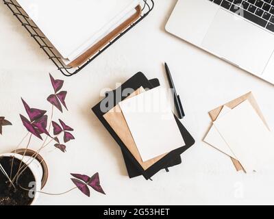 Home office desk with laptop, notebook, storage basket, purple houseplant, envelopes and postcards on white background. Flat lay, top view Stock Photo