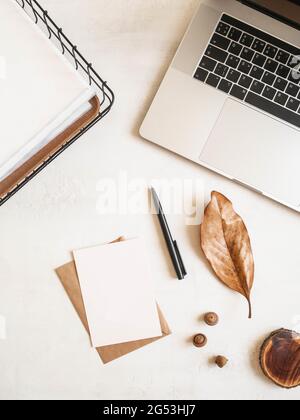 Home office desk with laptop, storage basket, dry leaf, acorns, envelopes and postcards on white background. Flat lay, top view Stock Photo