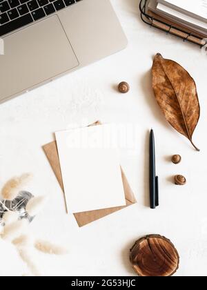 Home office desk with laptop, storage basket, dry flowers in vase, envelopes and postcards on white background. Flat lay, top view Stock Photo