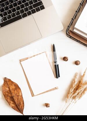 Home office desk with laptop, storage basket, dry flowers, envelopes and postcards on white background. Flat lay, top view Stock Photo