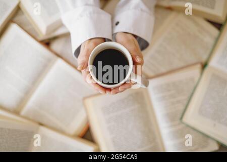 Top view of cup of coffee in woman hands on background of open books. Stock Photo