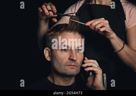 Portrait of handsome man with model haircut. New trendy modern hairstyle. Barber is shearing man hair. Midle-aged man in barbershop talking on the pho Stock Photo