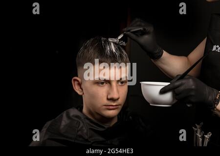 Handsome guy in barbershop. Young man with new haircut. Professional hairstyle. Model and trendy hairdressed. Barber is coloring male hair. Horizontal Stock Photo