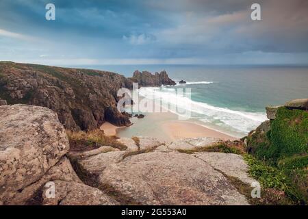 View from Treen Cliff over Pendvounder Beach near Porthcurno in Cornwall on a stormy summer morning, with the headland of Treryn Dinas in the distance Stock Photo