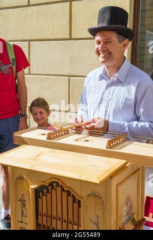 Ljubljana, Slovenia - August 15, 2018: An smiling street artist plays some traditional music for tourists in downtown with an old wooden instrument Stock Photo