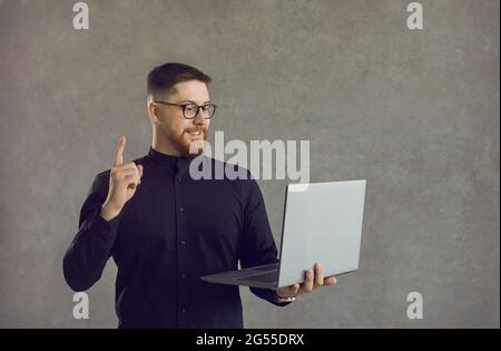Young man who's looking at screen of laptop has an idea, points finger up and smiles Stock Photo