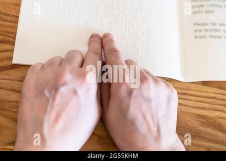point-of-view female fingers reading book with braille closeup on wooded table Stock Photo
