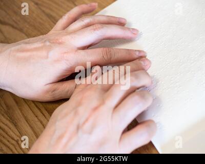 female hands reading book with braille closeup on wooded table Stock Photo