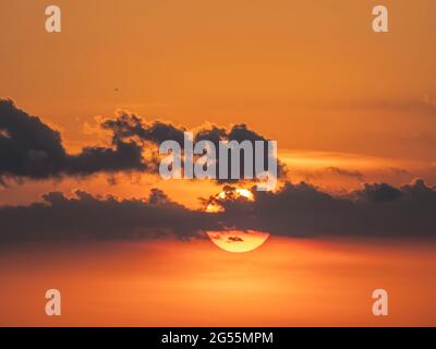Sun behind small clouds in orange sky near sunse Stock Photo