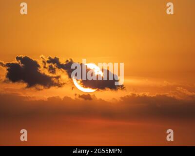 Sun behind small clouds in orange sky near sunse Stock Photo