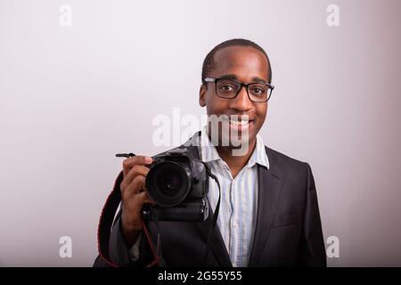 Smiling African photographer elegantly dressed with camera in hand. Model isolated on white background. Stock Photo